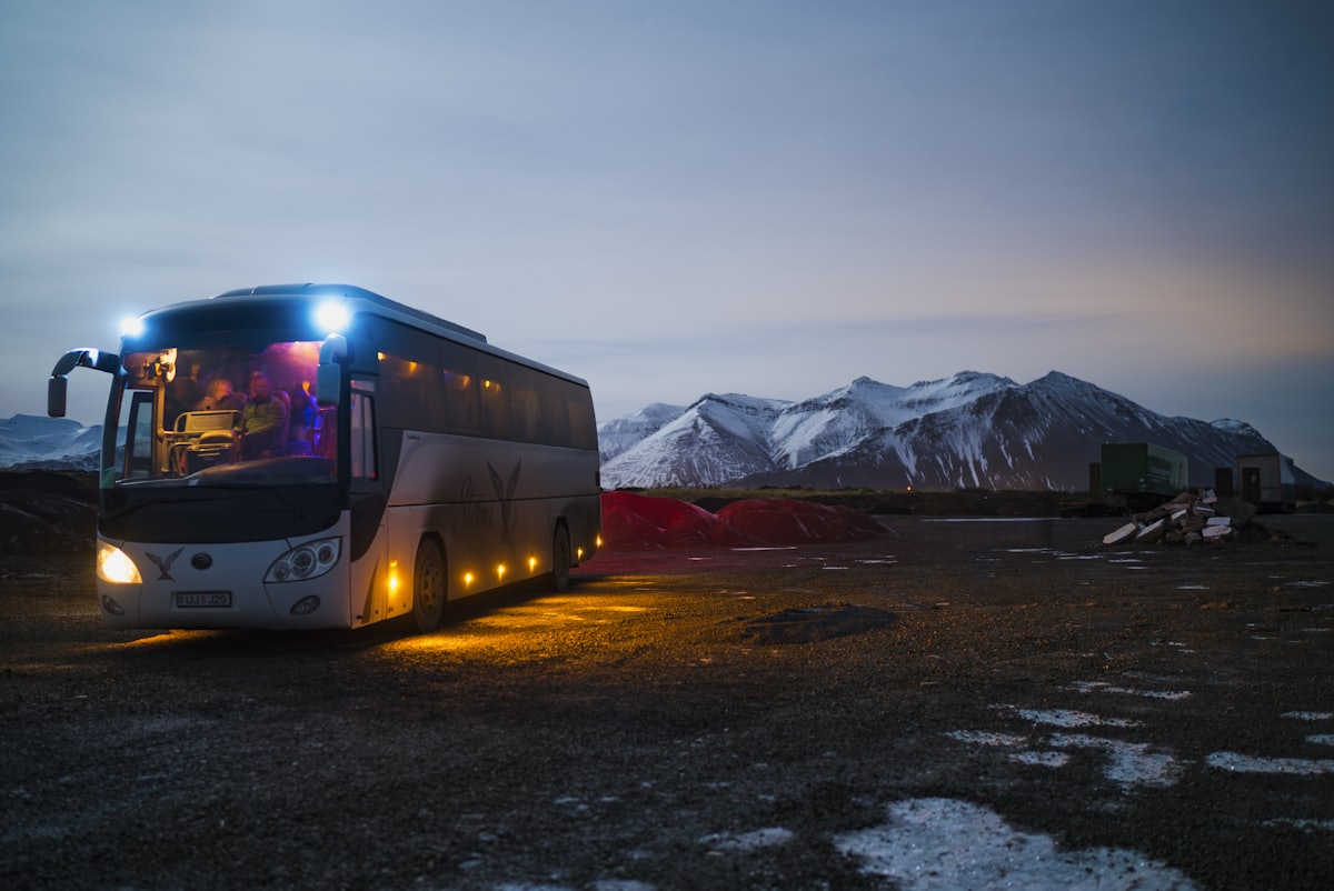 A coach waiting at dusk with its cabin lights on